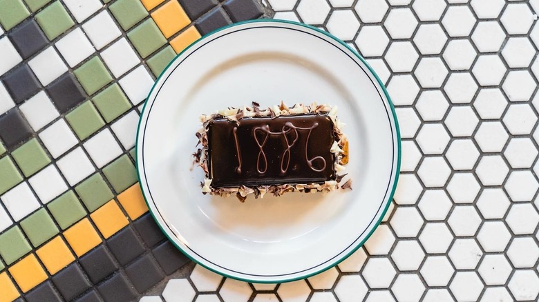 A rectangular chocolate cake with 1886 written in chocolate on top, sitting on a white saucer and a tile mosaic