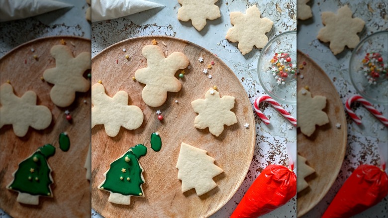 Wooden table is topped with a wooden plate that holds rolled sugar cookies decorated with green frosting