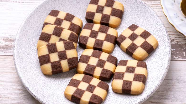 A wooden table with a gray plate is topped with black and white checkerboard cookies