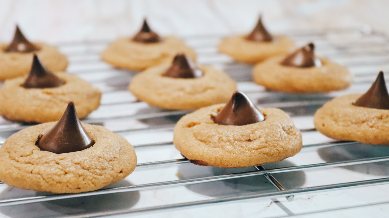 A metal wire rack holds several peanut butter blossom cookies, a peanut butter cookie base topped with a chocolate kiss candy