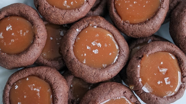 A close up of chocolate thumbprint cookies filled with a light brown caramel sauce and sprinkled with flaky salt