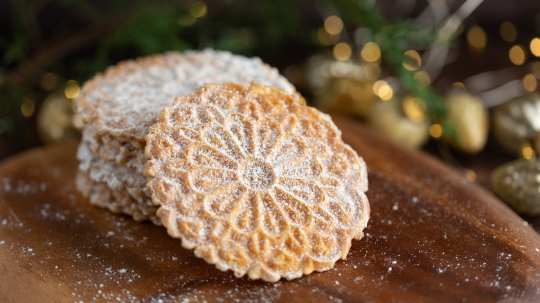 Italian pizzelle cookies dusted with powdered sugar on a wooden table with a Christmas tree in the background