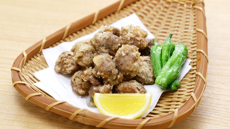 Breaded deep fried gizzards next to some peppers and a slice of lemon on a woven serving tray