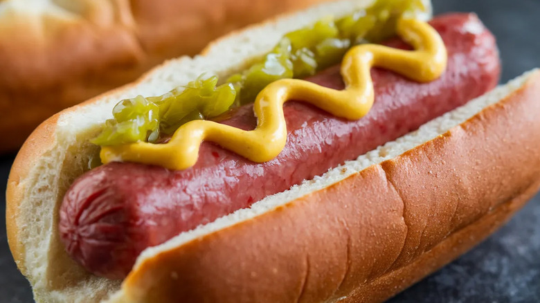 Close up of a hot dog on a bun topped with a squiggle of yellow mustard and some green relish