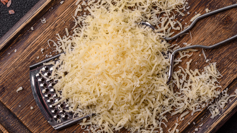 Parmesan cheese grated, with grater, on wooden board.