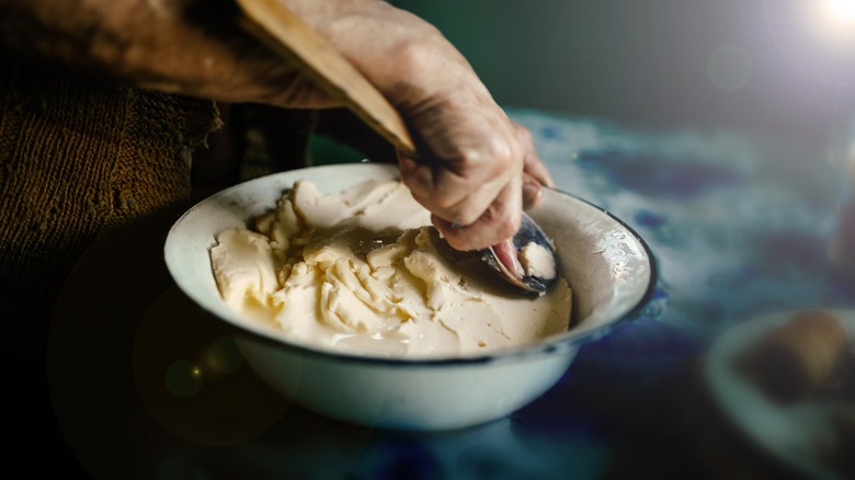 Close-up of person using a wooden spoon to shape homemade butter in a tin bowl