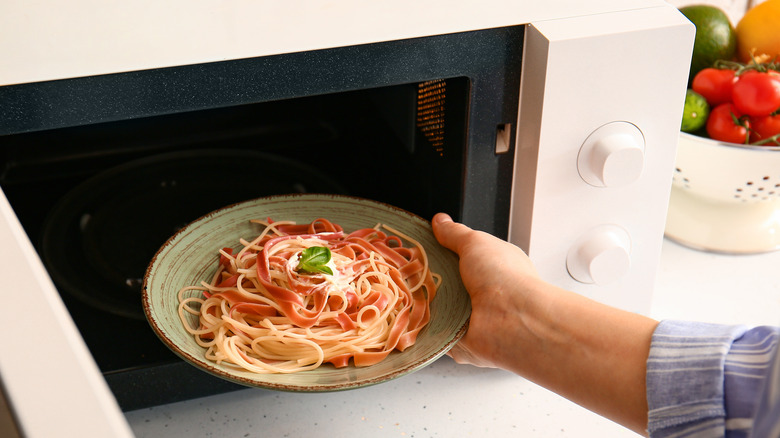 Hand placing pasta in microwave