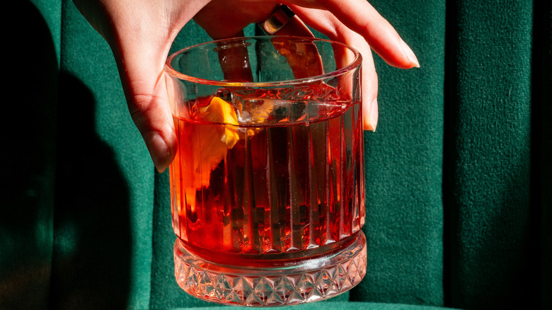 A hand lifts a negroni in front of green upholstery