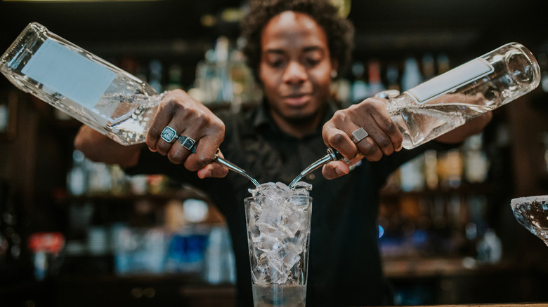 bartender pouring alcohol from two bottles into a glass at a bar