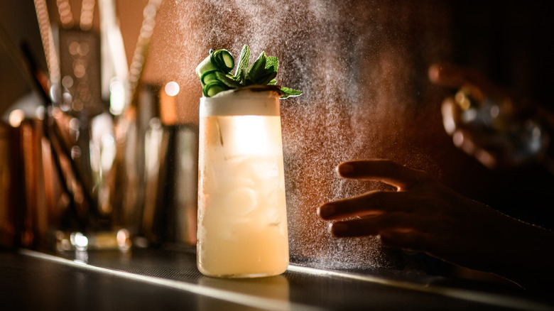 Hand reaching for a tall cocktail garnished with mint and cucumber