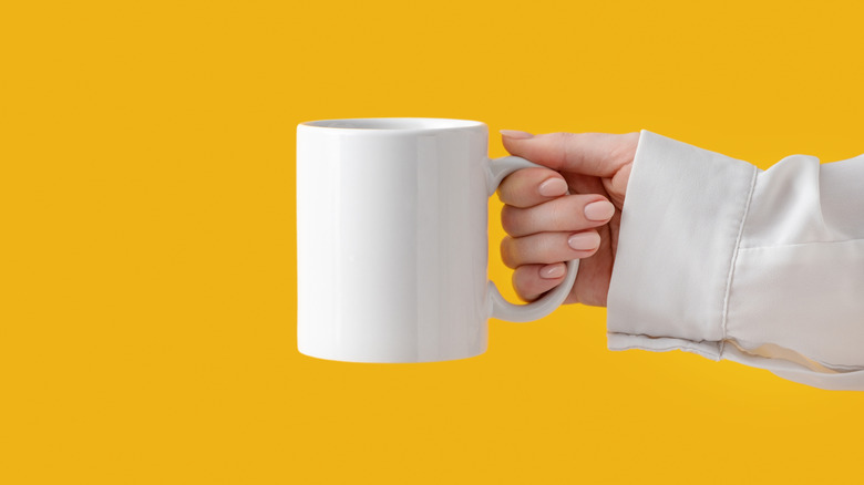person holding coffee mug yellow background