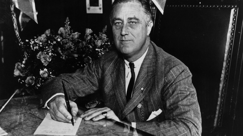 black and white image of Franklin D. Roosevelt at a desk signing paperwork