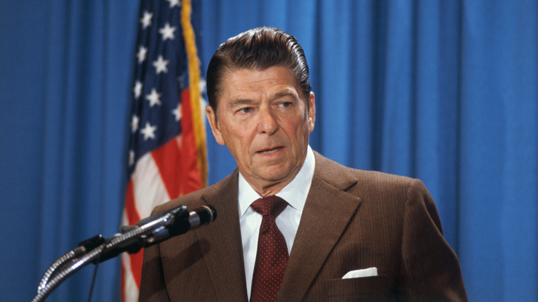Ronald Reagan with microphone in front of blue drapes and American flag