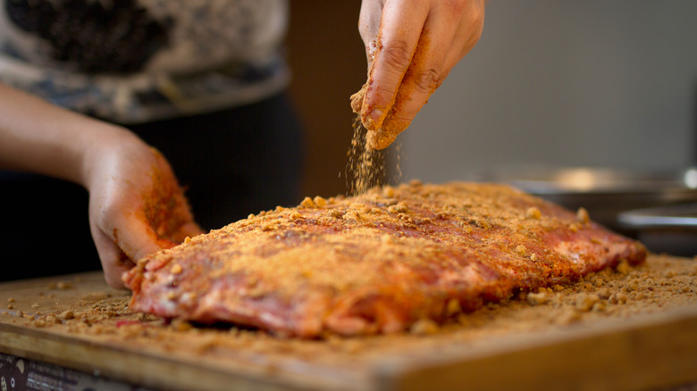 Hands sprinkling a dry rub on some pork ribs on a cutting board