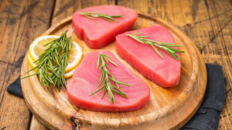 3 raw tuna steaks on a board with rosemary stalks and lemon slices