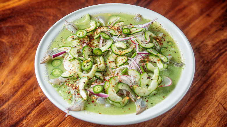 Aguachile with green sauce, sliced hot peppers, cucumber, red onion, and shrimp on white plate