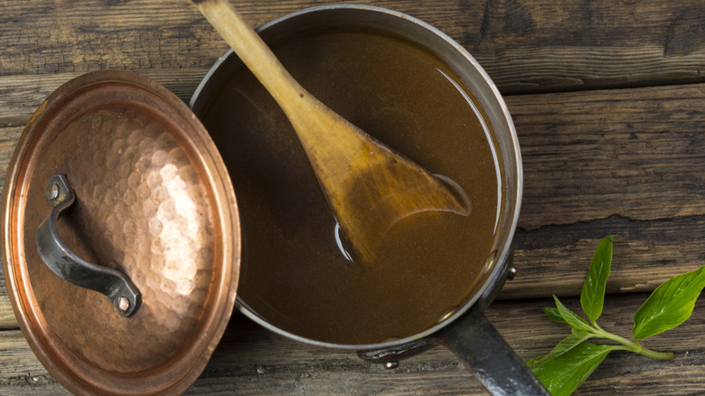 A pan filled with gravy and a wooden spoon on a wooden table