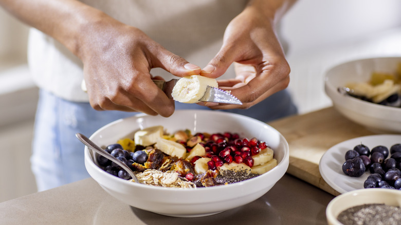 person slicing banana on top of bowl