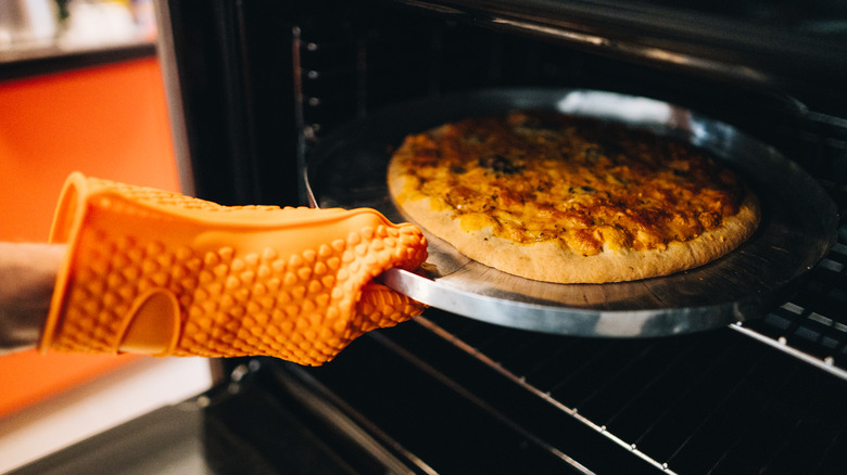 taking pizza out of oven with oven mitt