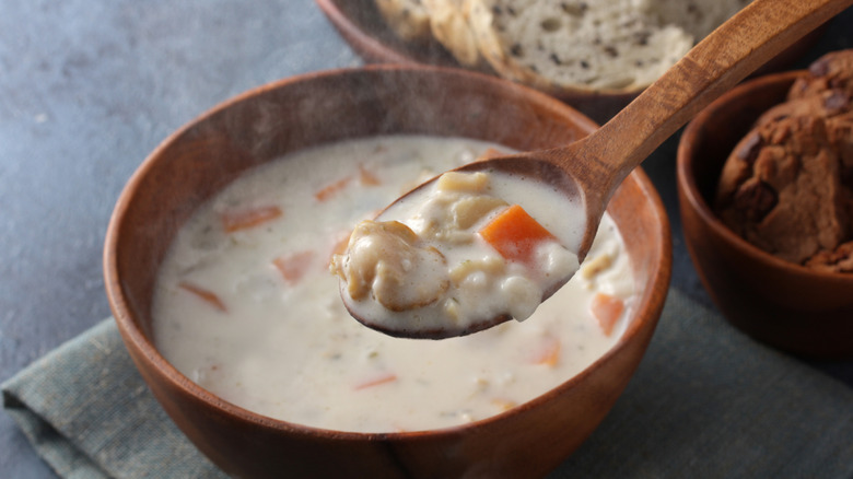 A spoon of clam chowder hovering over a bowl