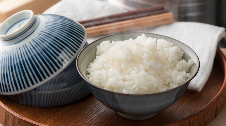 A steaming bowl on rice on a wooden tray with a napkin and chopsticks
