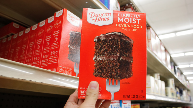 A hand holding Duncan Hines devil's food cake mix in a grocery store aisle