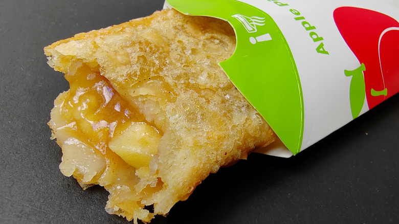 A McDonald's apple pie in its cardboard sleeve with a bite taken out of it, exposing its apple filling