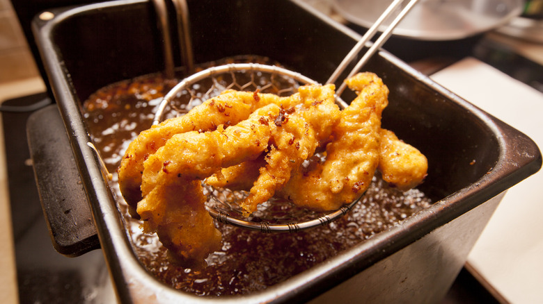 Lifting deep-fried chicken tenders out of hot oil with metal strainer