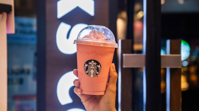 Someone holding a Starbucks strawberry Frappuccino topped with whipped cream in a clear plastic cup
