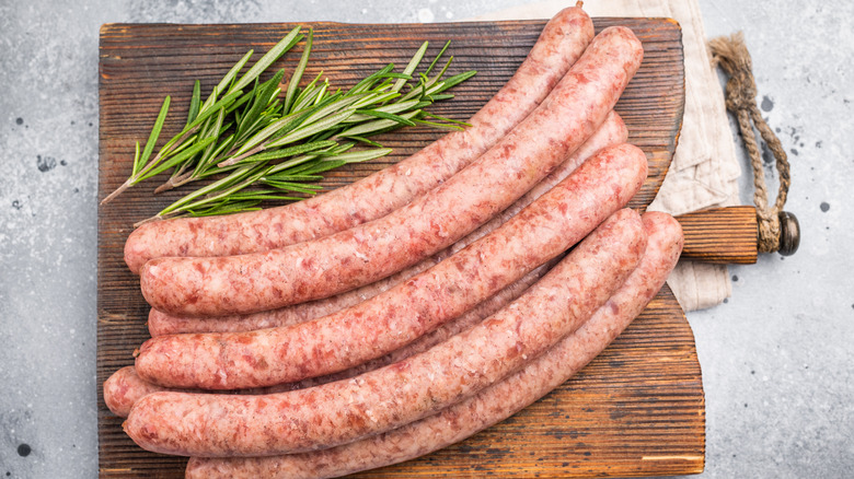 A cutting board with raw, fresh sausages next to some rosemary