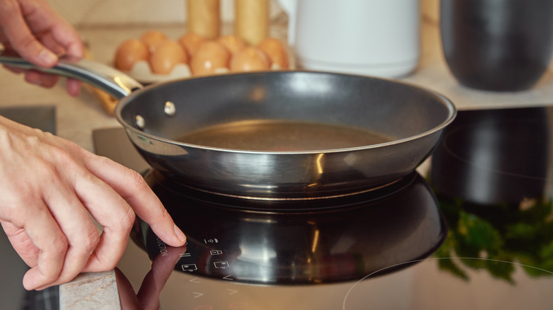 A person presses buttons on an induction stove with a steel frying pan on a burner