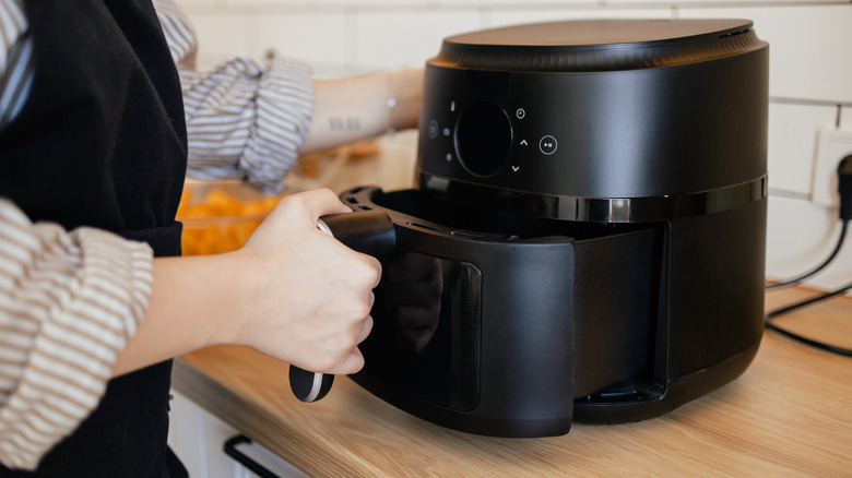 Someone opening up an air fryer on a countertop