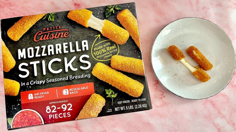 A box of Petite Cuisine mozzarella sticks on a counter next to a plate with two mozzarella sticks on it