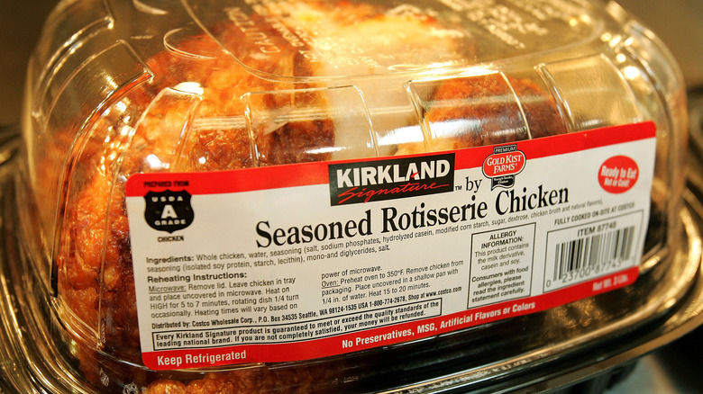 A plastic clamshell package containing a ready-to-eat Kirkland Signature Seasoned Rotisserie Chicken