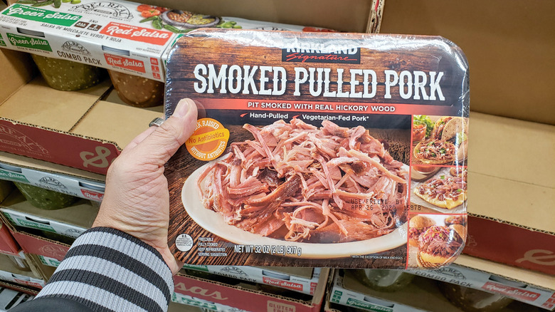 A person holding a package of Kirkland Signature Smoked Pulled Pork in a Costco warehouse