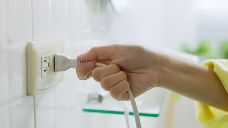 A close up of a woman unplugging a power cord from an outlet