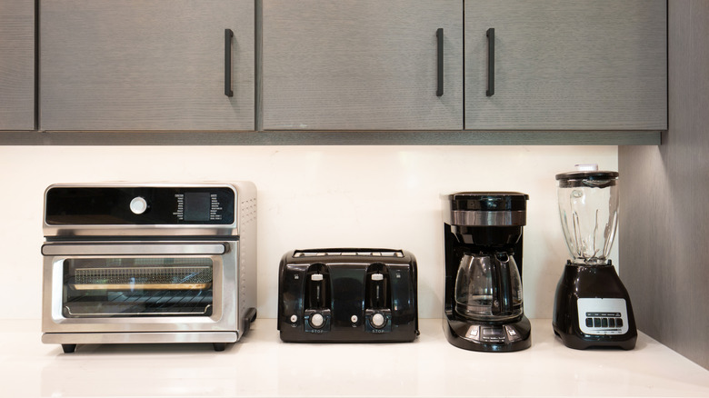 A toaster oven, toaster, coffee maker, and blender lined up on a kitchen counter