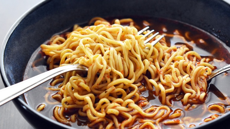 A black bowl filled with instant ramen, a fork, and a spoon