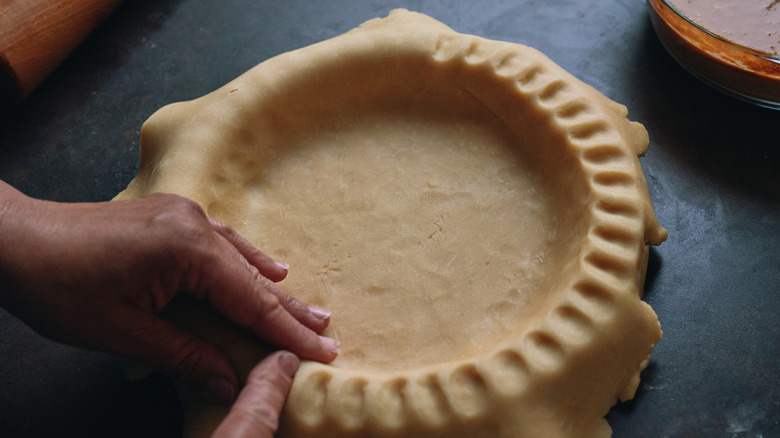 hands crimping a pie crust into a dish