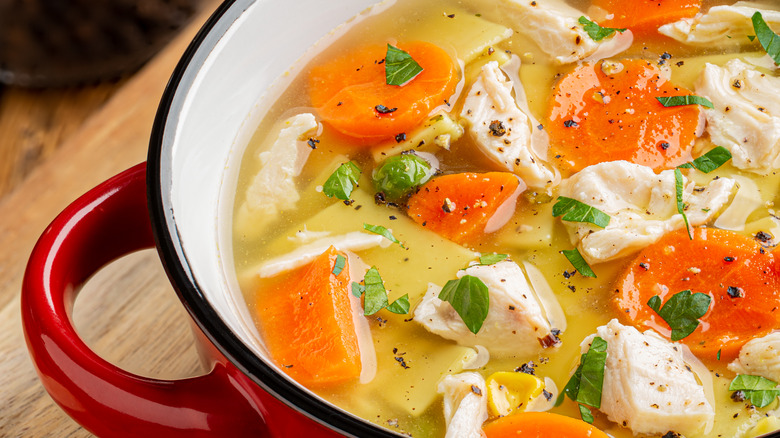 closeup of chicken noodle soup with carrots and herbs ina red handled pot