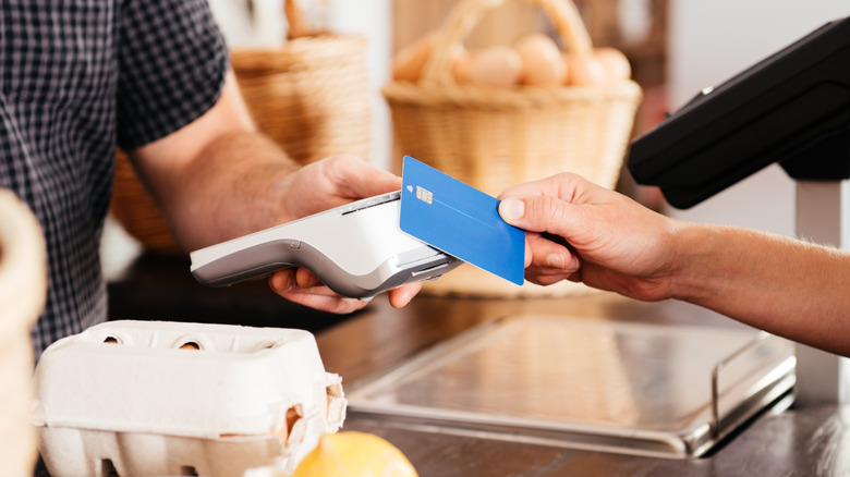 A man tapping a blue credit card to buy eggs at the grocery store