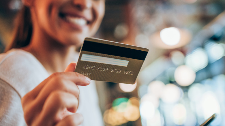 A woman and smiling while holding and looking at a credit card