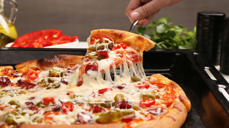 a hand lifting a slice of pizza out of a whole one, the cheese pull still connecting them