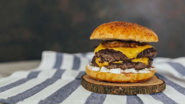 A cheeseburger layered with sauce, two patties, and bacon sitting on a striped tea towel