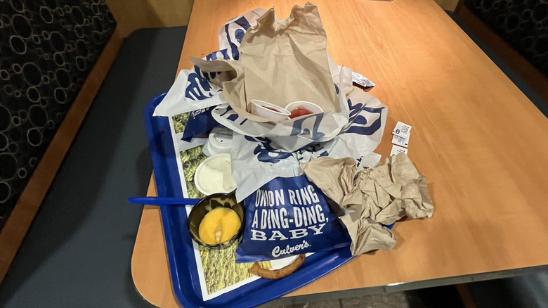 Table inside Culver's restaurant with messy blue tray on top holding garbage, cup of cheese sauce, napkins, and ketchup cups