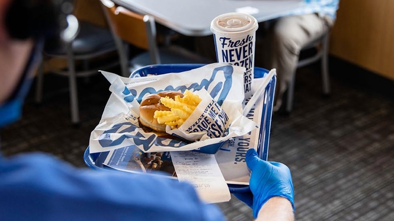 An employee holding a tray of Culver's food with a burger, fries, and a drink.