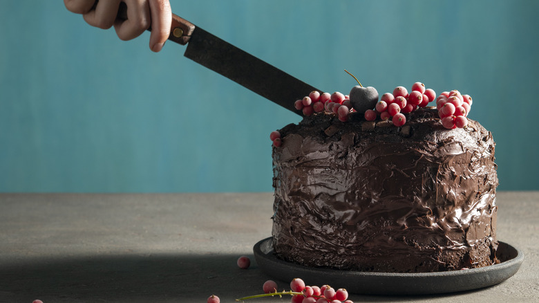 hand cutting a tall chocolate cake