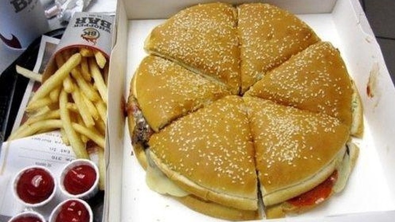 A Burger King Pizza Burger cut into six slices in its box beside french fries and paper cups of ketchup