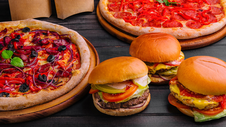 Burgers and pizzas laid out together on a dark wood table