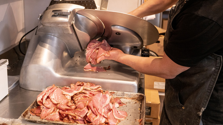 Deli worker uses a meat slicer on cold cuts